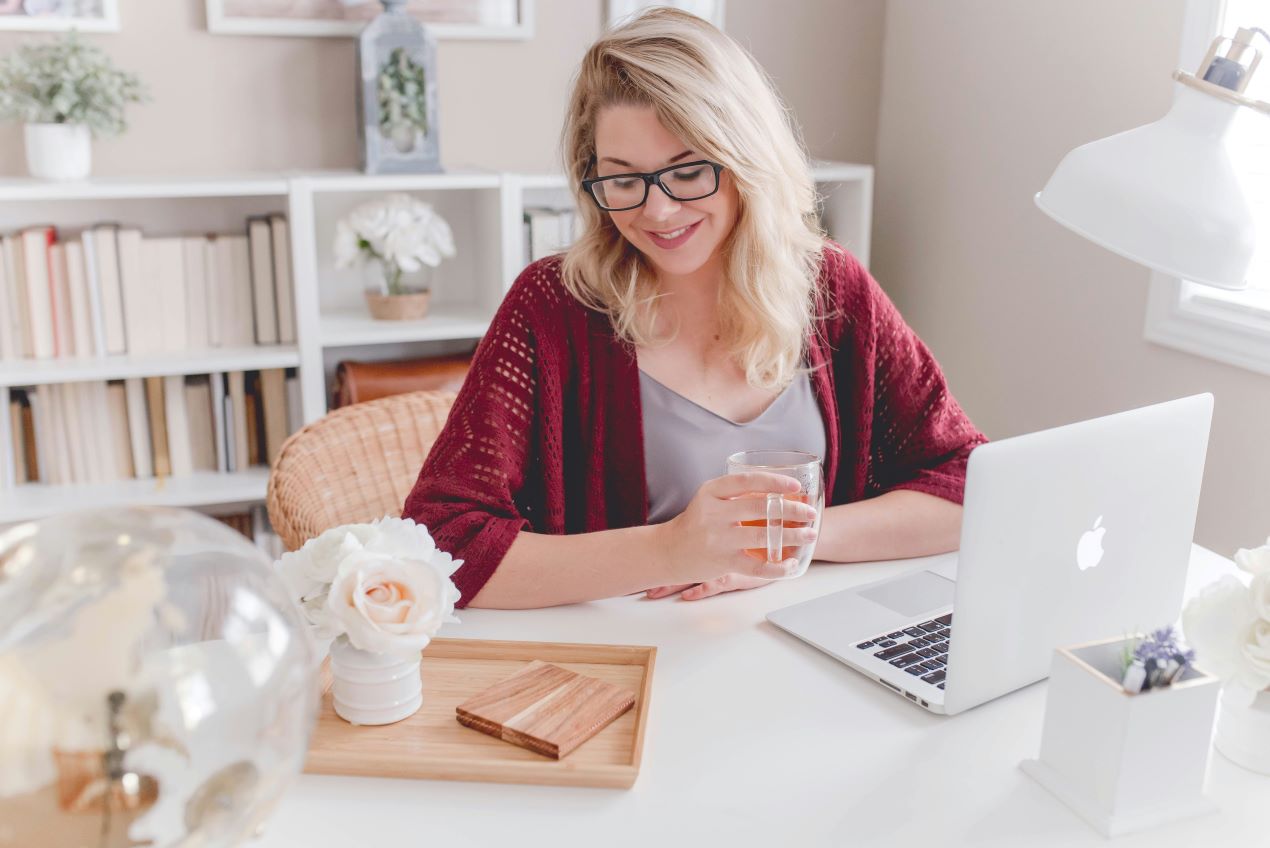 Frau am Laptop mit Tee in modernem Büro, plant ihre Fotos digitalisieren zu lassen.