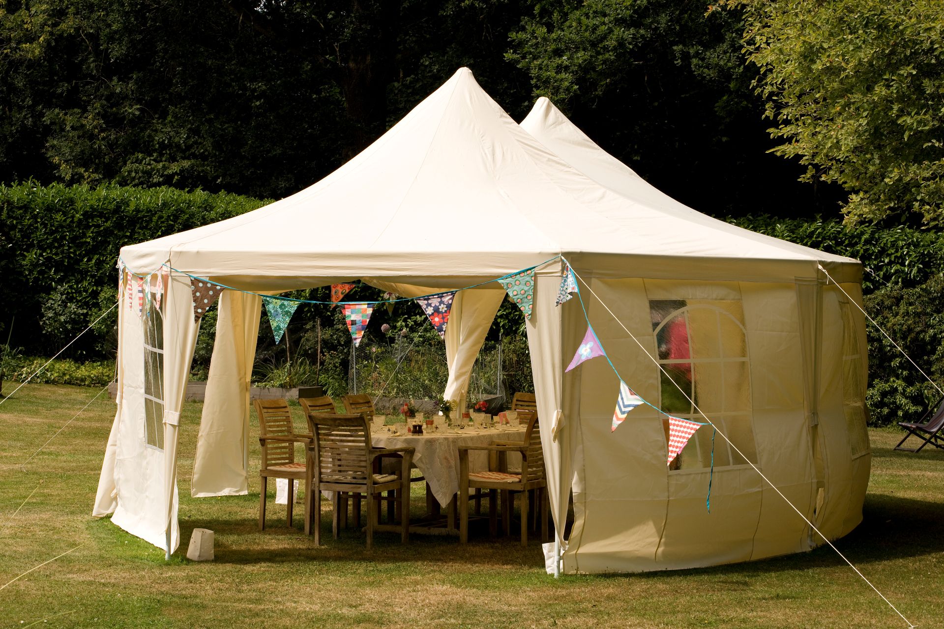 Pavillon mit Holztischen und -stuehlen, bunte Wimpelketten und festliche Dekoration im Garten
