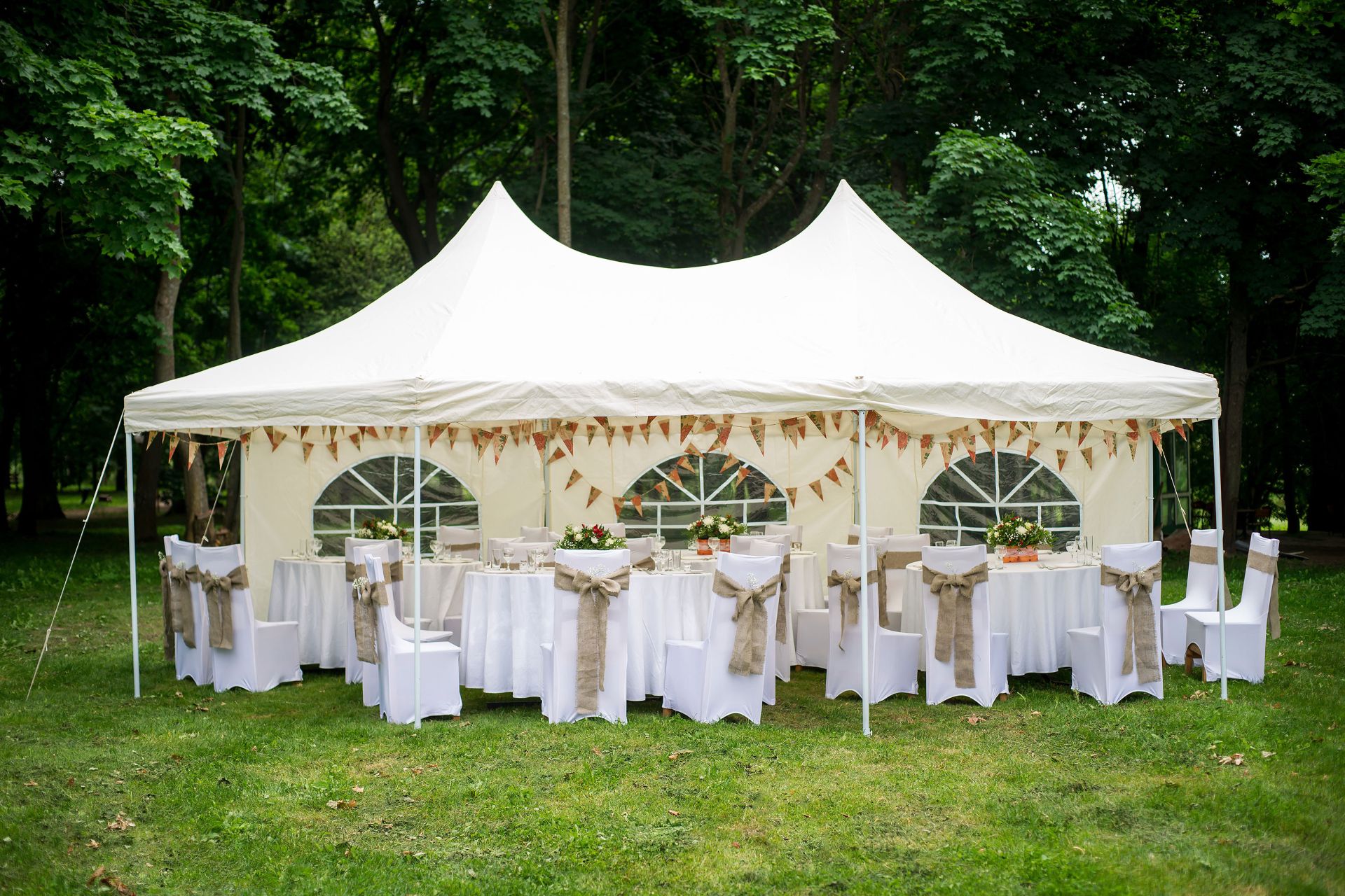 Grosser Pavillon mit weissen Stuhlhussen, festlich gedeckter Tafel und Wimpelketten im Garten