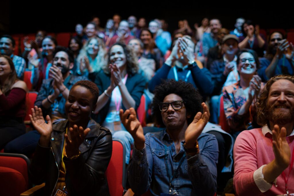 Zahlreiche Personen sitzen in einem Veranstaltungssaal und applaudieren nach einem Event mit Moderation